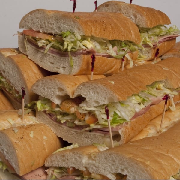 A close-up of several large submarine sandwiches, cut in half, filled with meat, cheese, lettuce, and tomatoes.