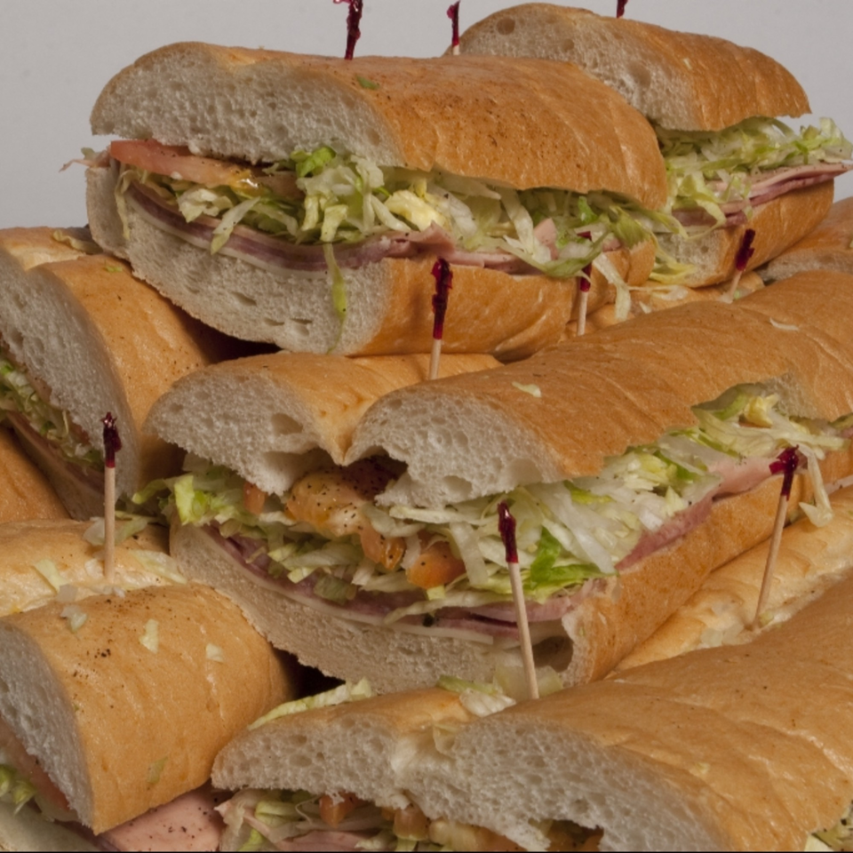A close-up of several large submarine sandwiches, cut in half, filled with meat, cheese, lettuce, and tomatoes.