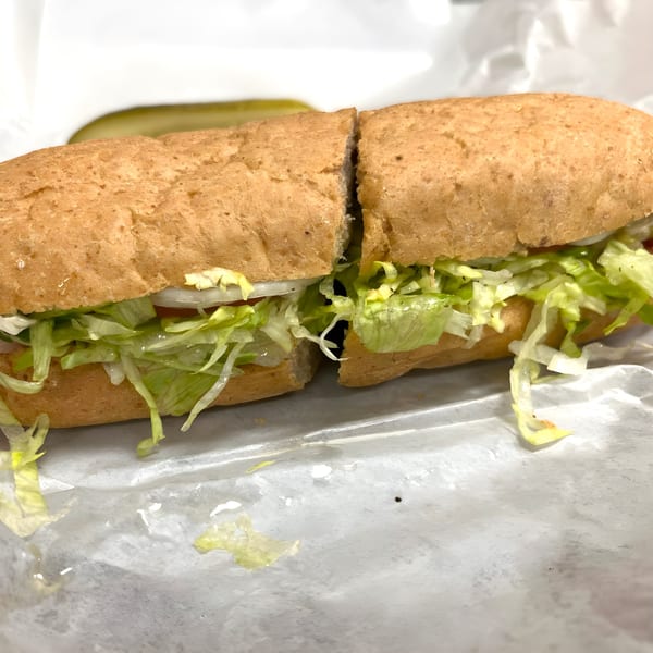 Ned's Krazy Sub sandwich, cut in half, with lettuce, onion, and tomato, on white paper.