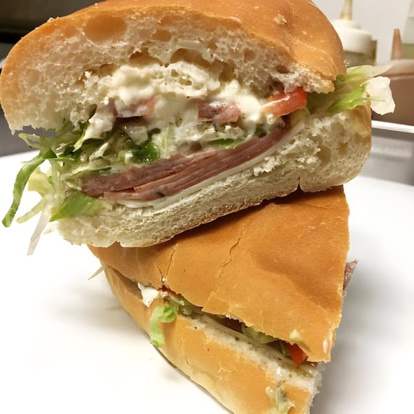 A Ned's Krazy Sub sandwich, cut in half, revealing layers of meat, cheese, lettuce, tomato, and sauce.