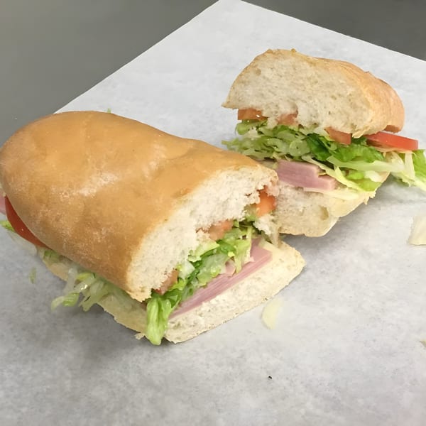 A Ned's Krazy Sub sandwich, cut in half, revealing ham, lettuce, and tomato on a white paper.