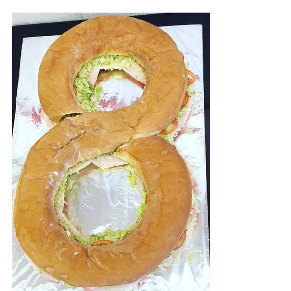 A large sub sandwich shaped like the number eight, filled with lettuce, tomatoes, and deli meat.
