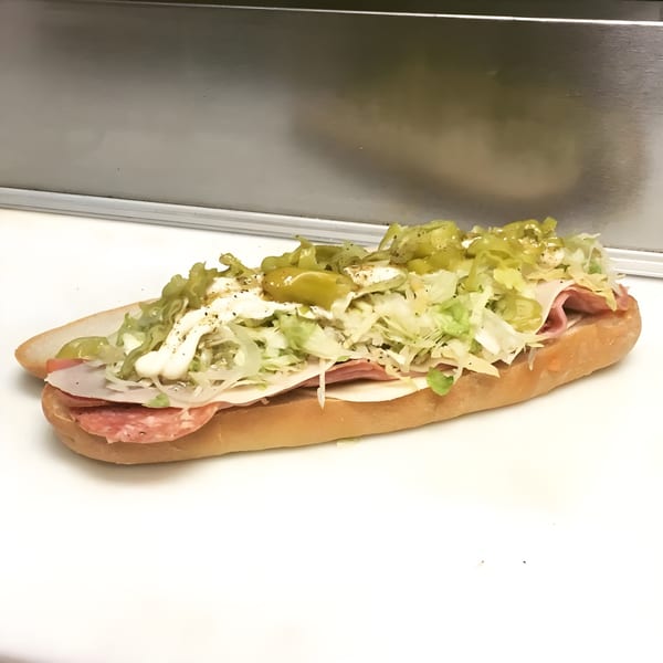A Ned's Krazy Sub sandwich with salami, cheese, lettuce, and peppers on a white surface.