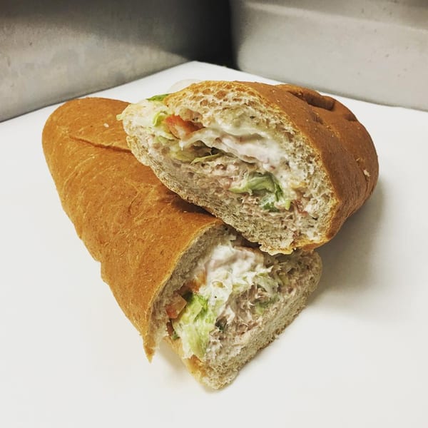 A Ned's Krazy Sub sandwich, cut in half, revealing tuna salad, lettuce, and tomatoes.